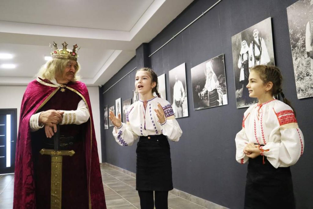 Two girls in traditional Moldovan dress perform a story with the help of an actor playing a King.