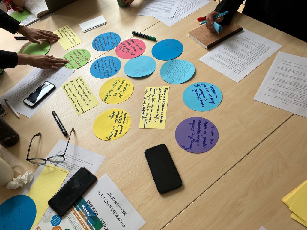 Fourteen ideas written on colourful pieces of table are on a table. They are surrounded by other pieces of paper and paraphernalia from a meeting.
