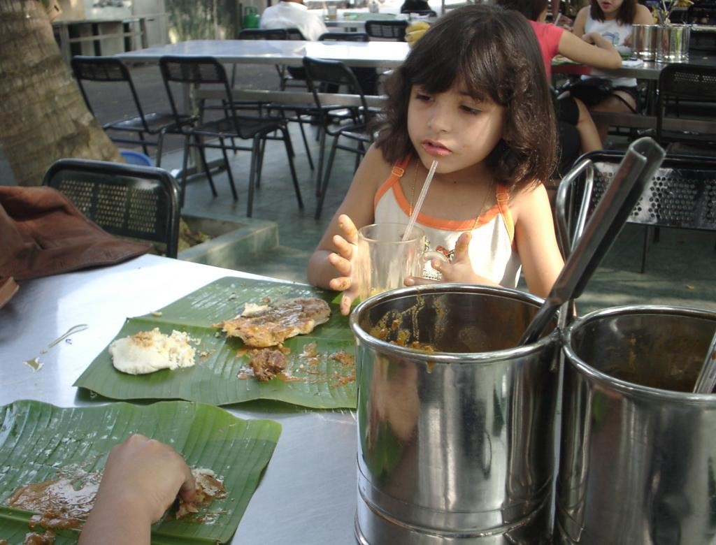 A young girl eating Malaysian food served on a banana leaf. 