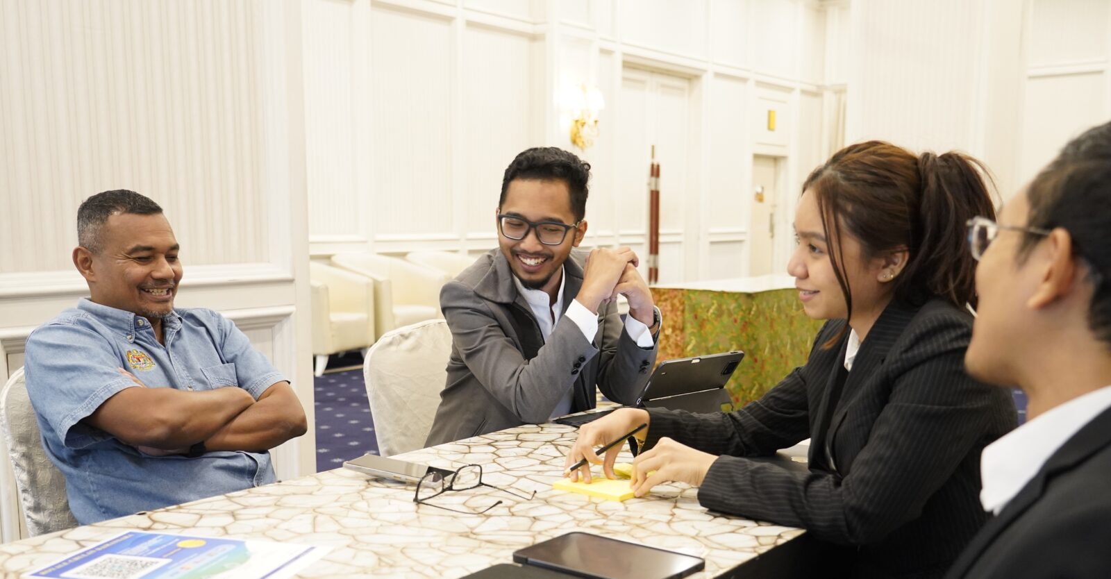 Three men and a woman dressed in business attire sat at a table. They are smiling and talking.