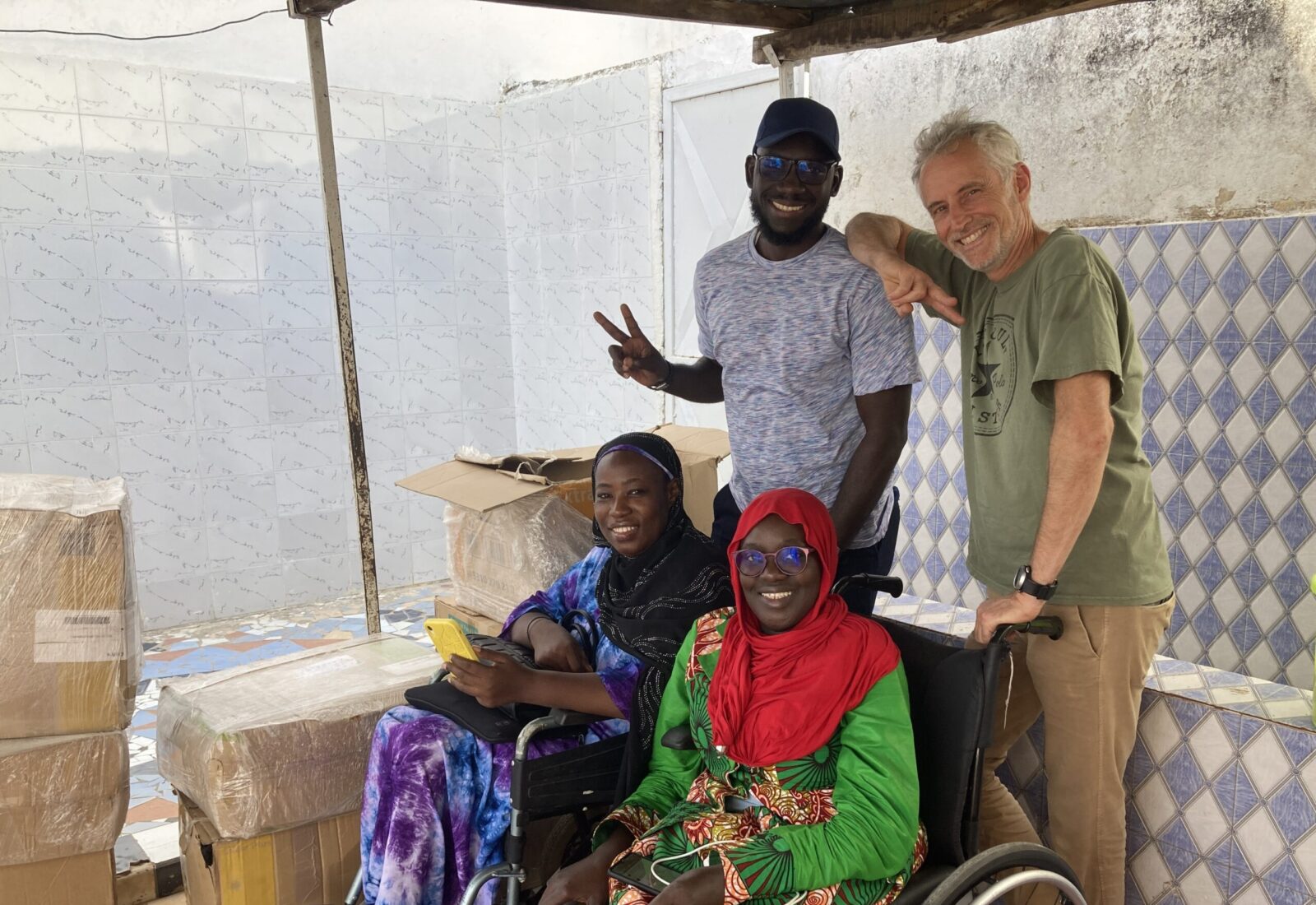 Four people smiling at the camera in front of boxes. Two people are in wheelchairs, while the other 2 are standing.