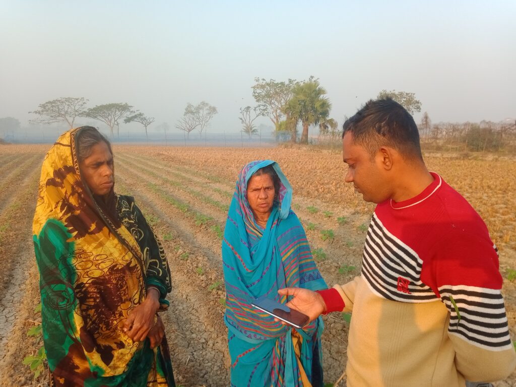 Two women and a man standing in a field looking at a smartphone.